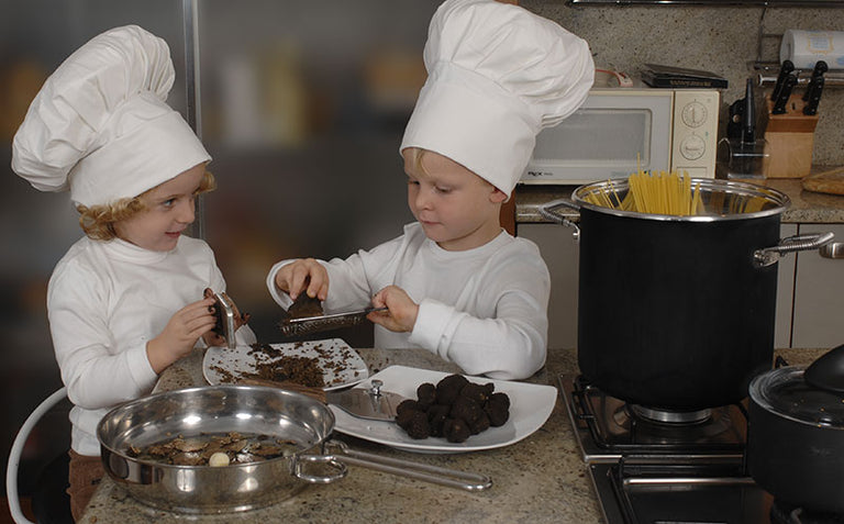 Two children in chef's whites shaving truffles in a kitchen